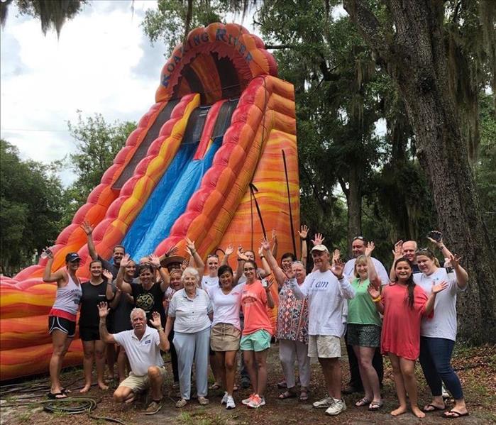 Large 24ft orange waterslide in the background with group of people standing in front posing to show the height of the slide.