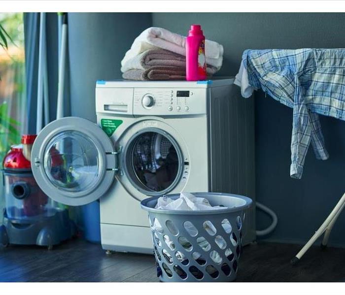 Dryer door open in a laundry room with pink detergent. 