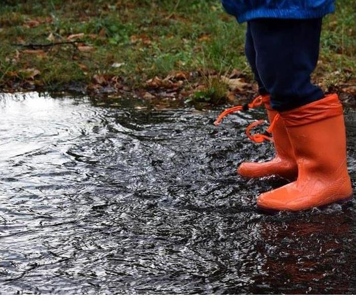 A person is shown walking through a puddle in orange rain boots