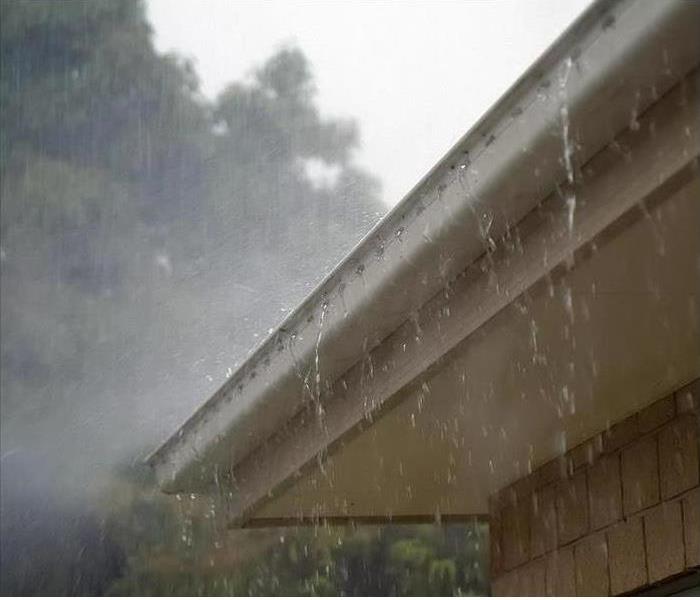 A gutter is shown overflowing due to heavy rainfall